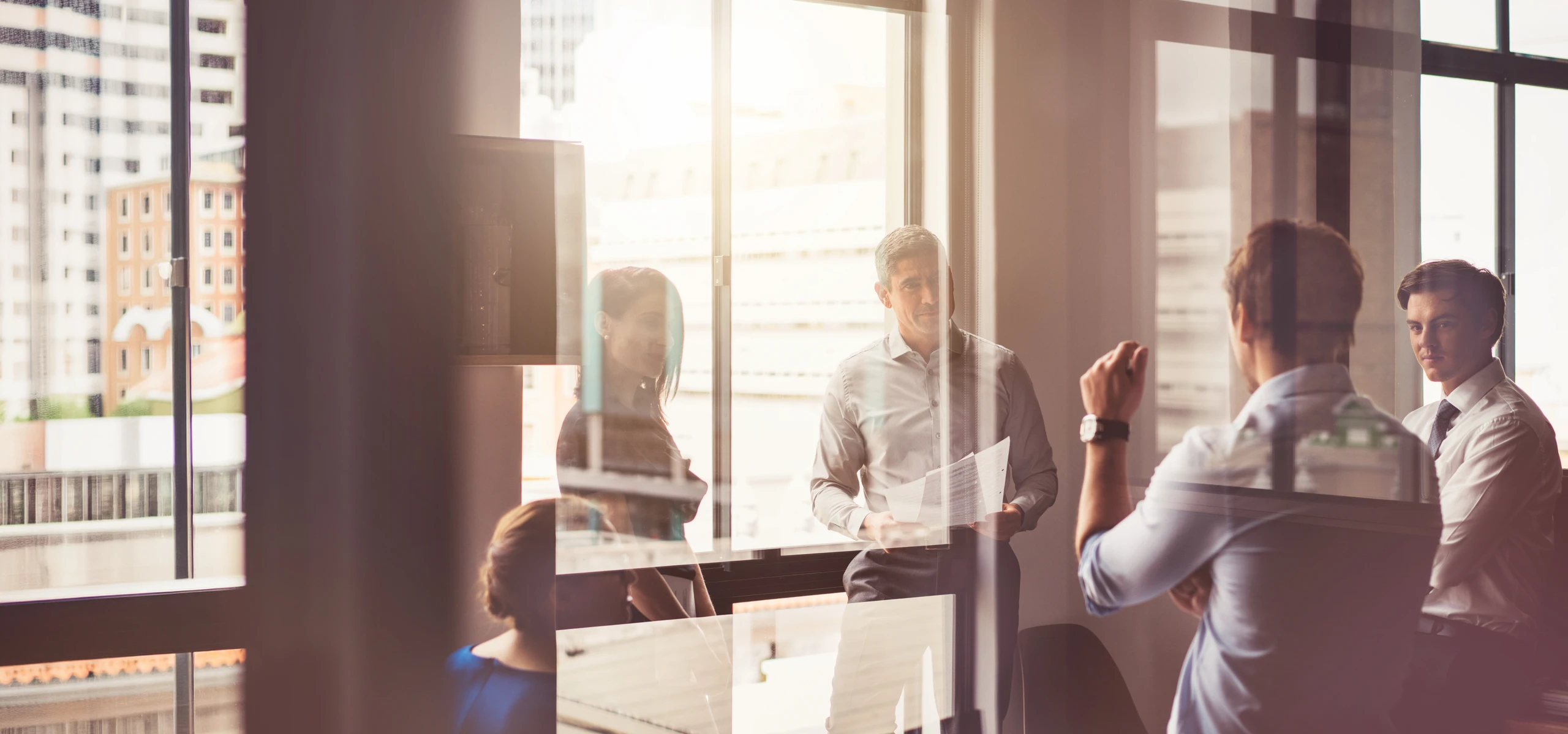 Small group discussing documents during a meeting in a glass-walled office.